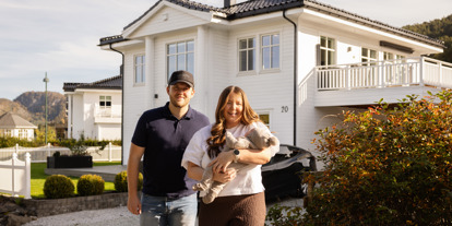 Par med baby i hendene, fremfor en hvit, stor enebolig. 