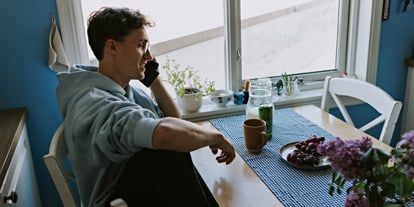 Mann sitter ved et kjøkkenbord, snakker i telefonen.