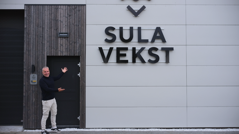 Mann står ved inngangen til en moderne bygning med skiltet «Sula Vekst».