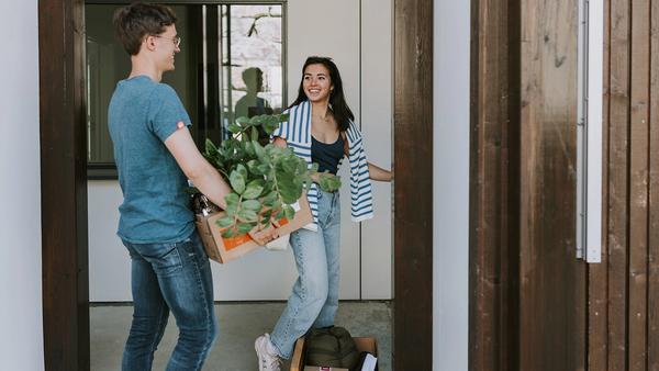 Mann bærer en eske med planter, dame smiler ved døren