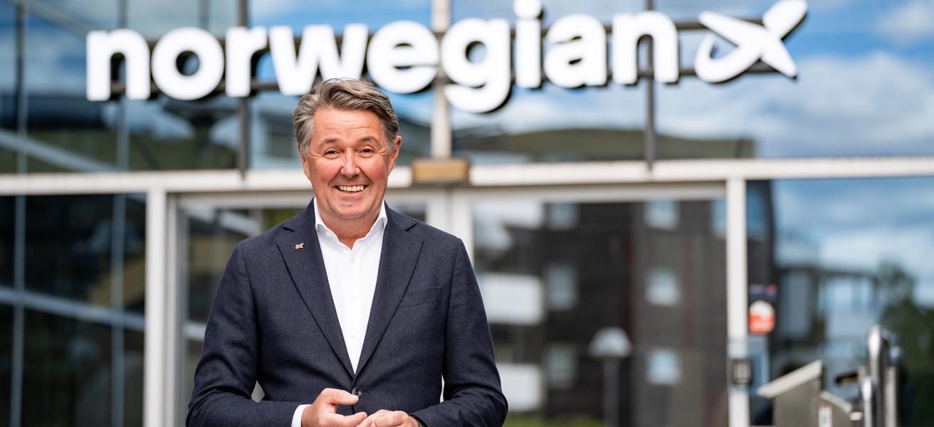 Mann i dress og hvit skjorte står fremfor et forretningsbygg. Norwegian-logo på bygget