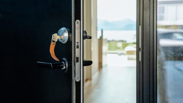 Svart ytterdør som står på gløtt med nøkkelen i.