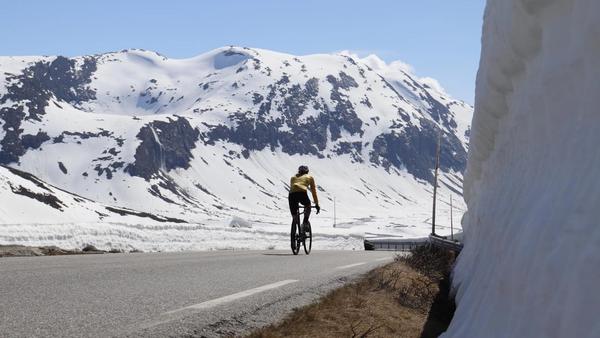 Sykkelturist på fjellvei omgitt av snø, Sunnmøre, en del av trenden Coolcation som forlenger reiselivssesongen på Nordvestlandet.