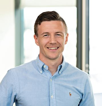 Ung mann kledd i blå skjorte, smiler til kamera