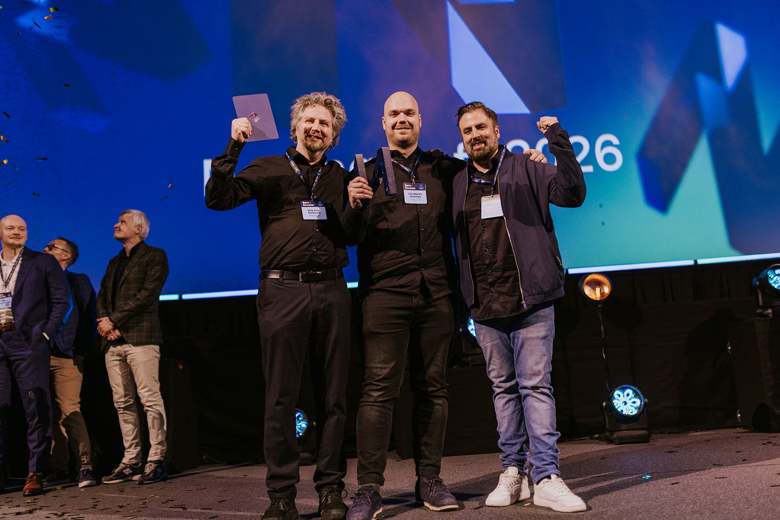 Flere som holder en pokal og jubler, på en scene. 
