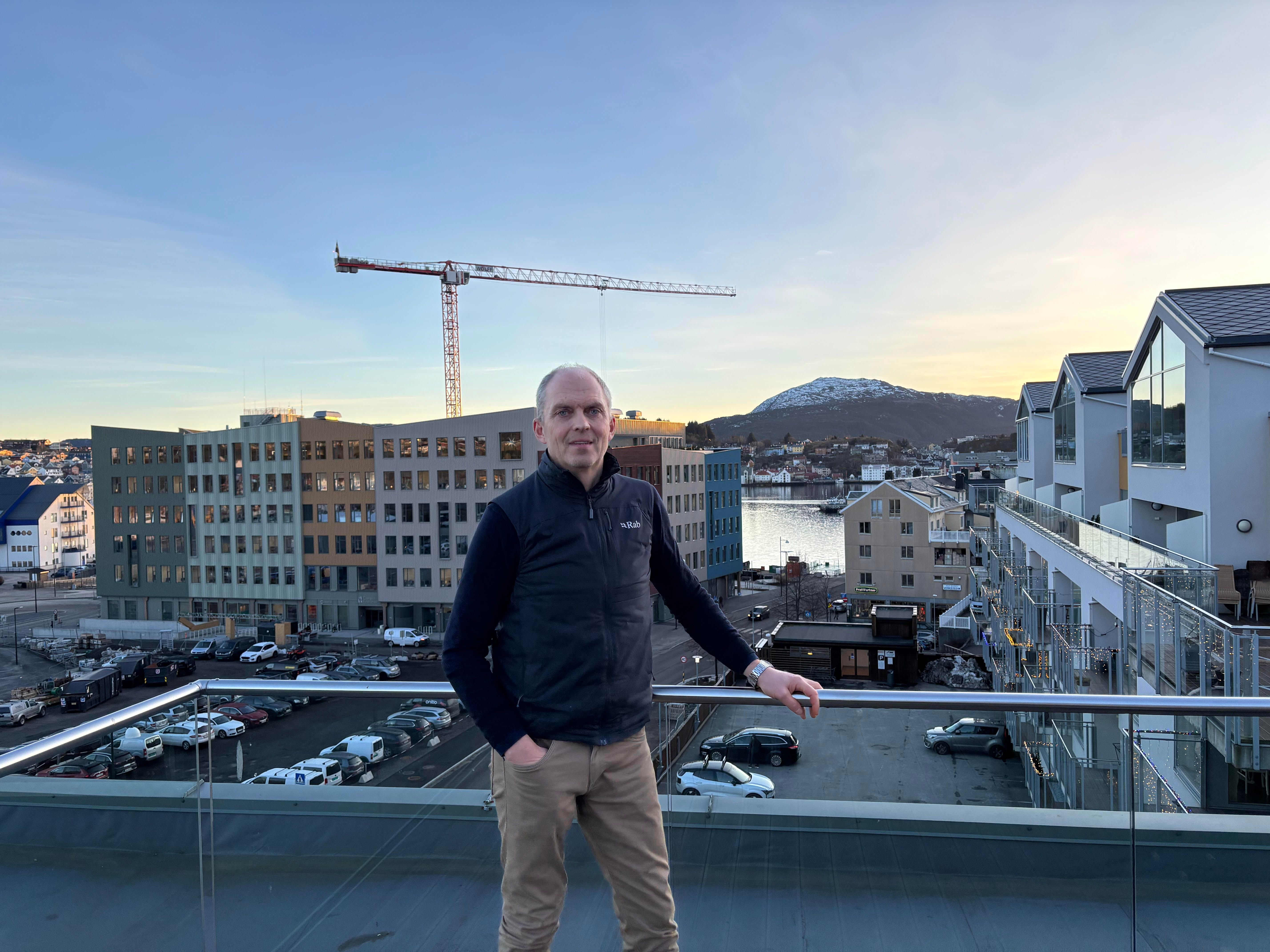 En mann står på en takterrasse med utsikt over et byutviklingsområde med nye bygg, byggekran og nærliggende bebyggelse.