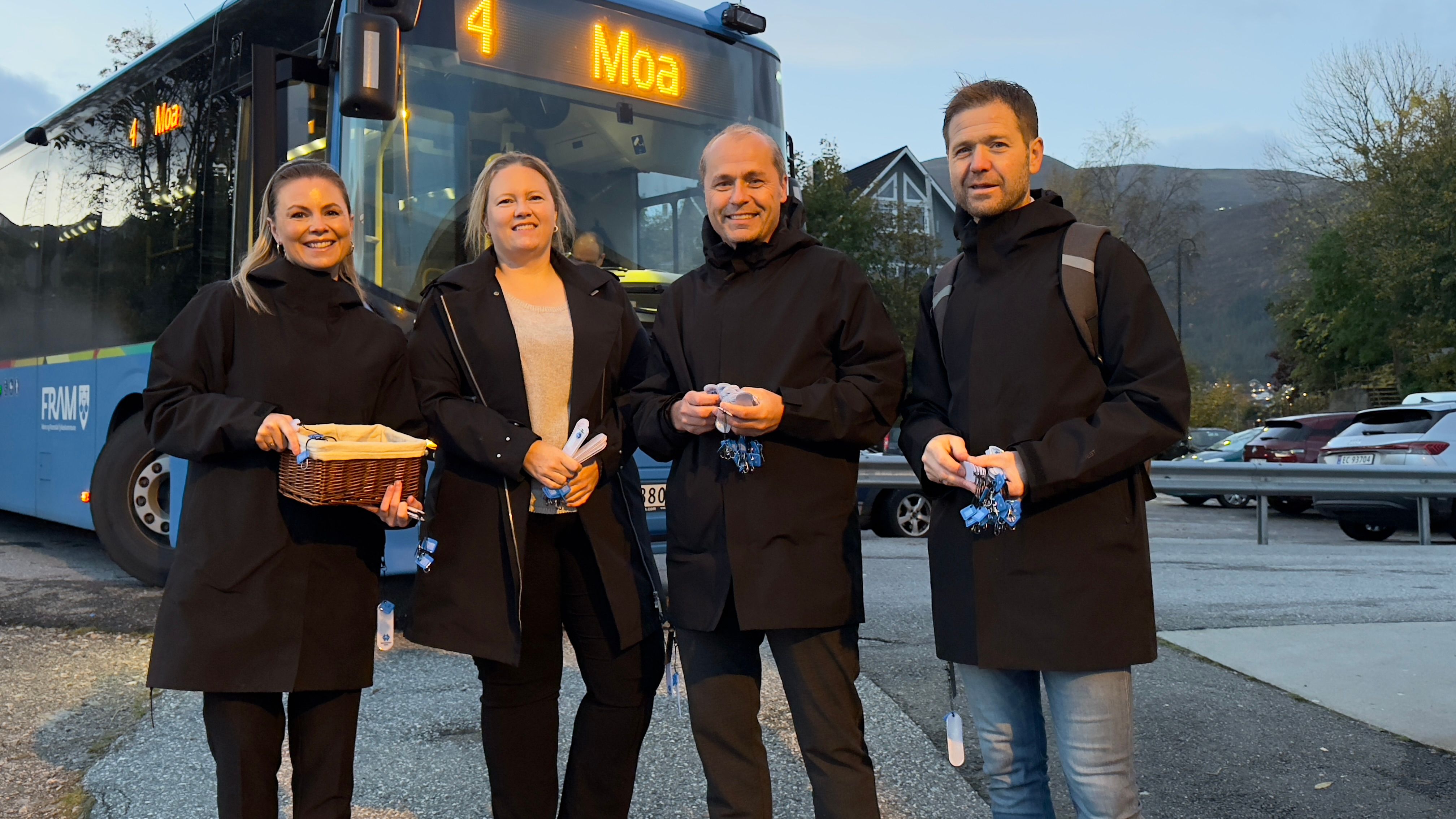 To kvinner og to menn i sorte jakker med refleks i hendene. Står sammen med en buss i bakgrunn.