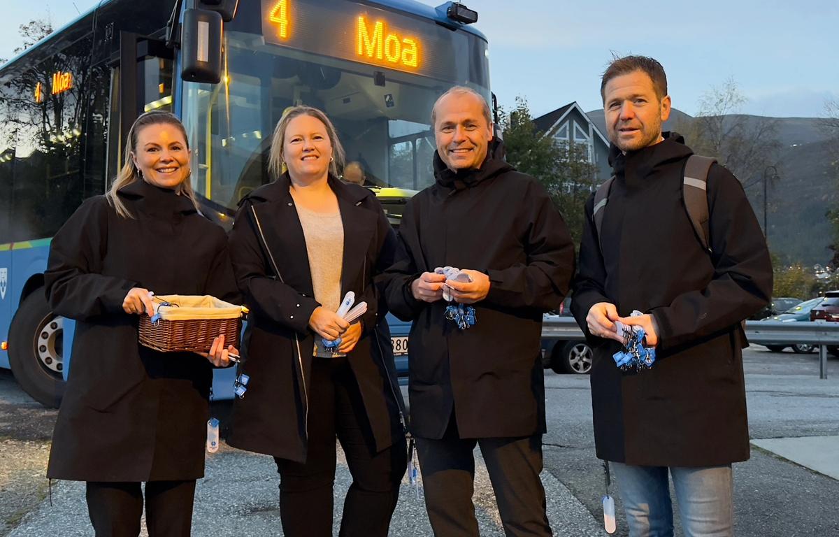 To kvinner og to menn i sorte jakker med refleks i hendene. Står sammen med en buss i bakgrunn.