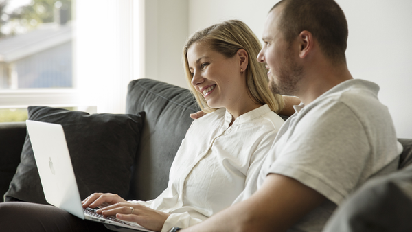 Et par som sitter i sofaen og ser sammen på en laptop.