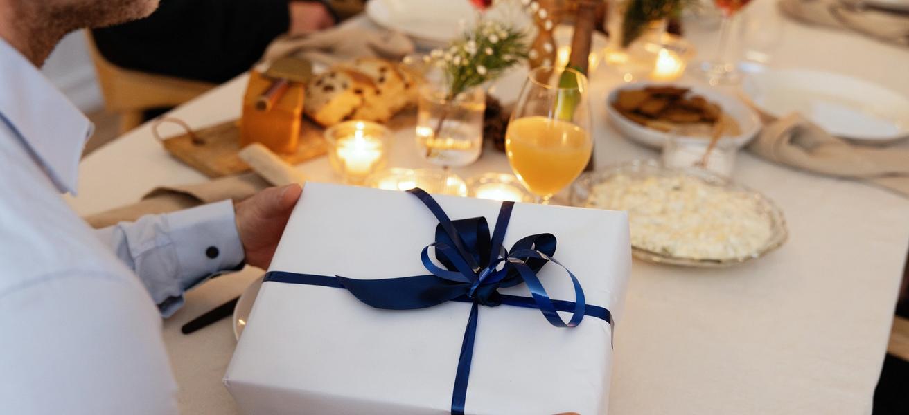 Juledekket bord med en julegave pakket i hvitt papir og blått bånd.
