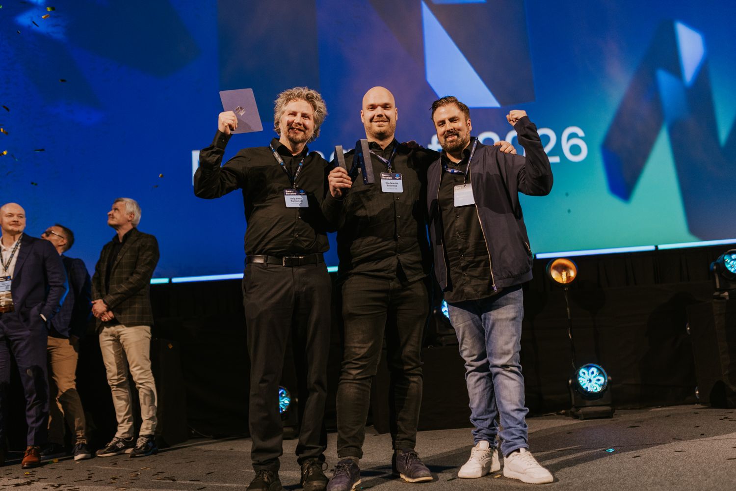 Flere som holder en pokal og jubler, på en scene. 