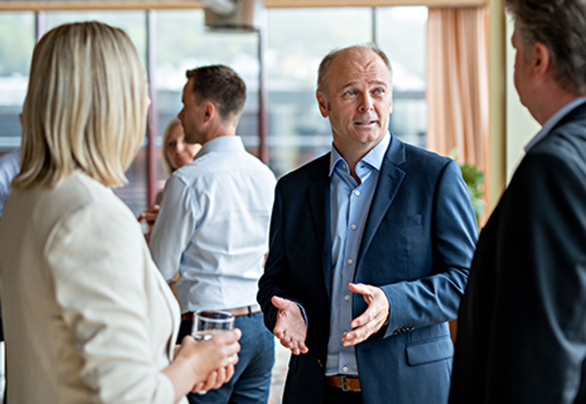 Flere mennesker i minglesituasjon. Mann i dress står i midten og er i fokus i bildet.