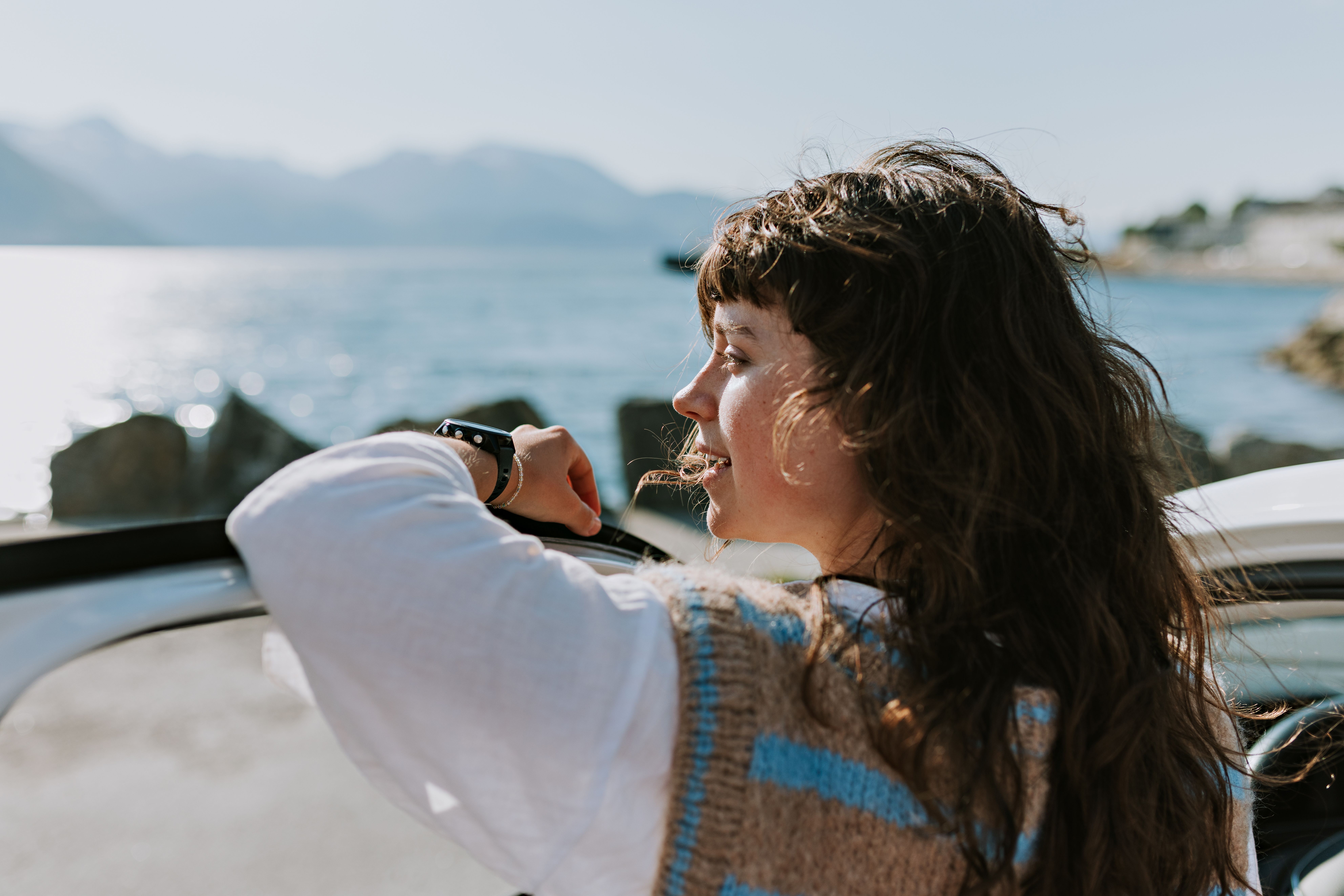 Jente som lener seg på bildør og ser ut mot havet. 