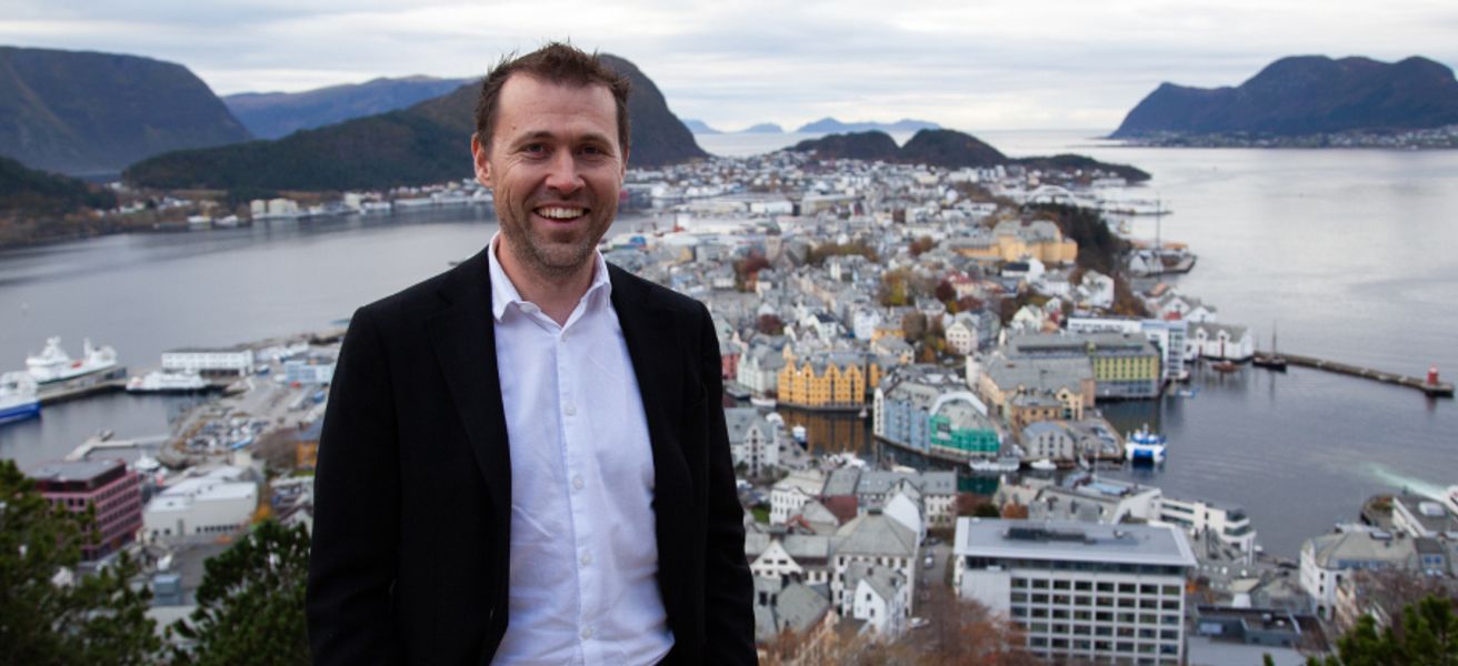 Jan Tore Holen smiler foran utsikt over Ålesunds bysentrum og fjordlandskap