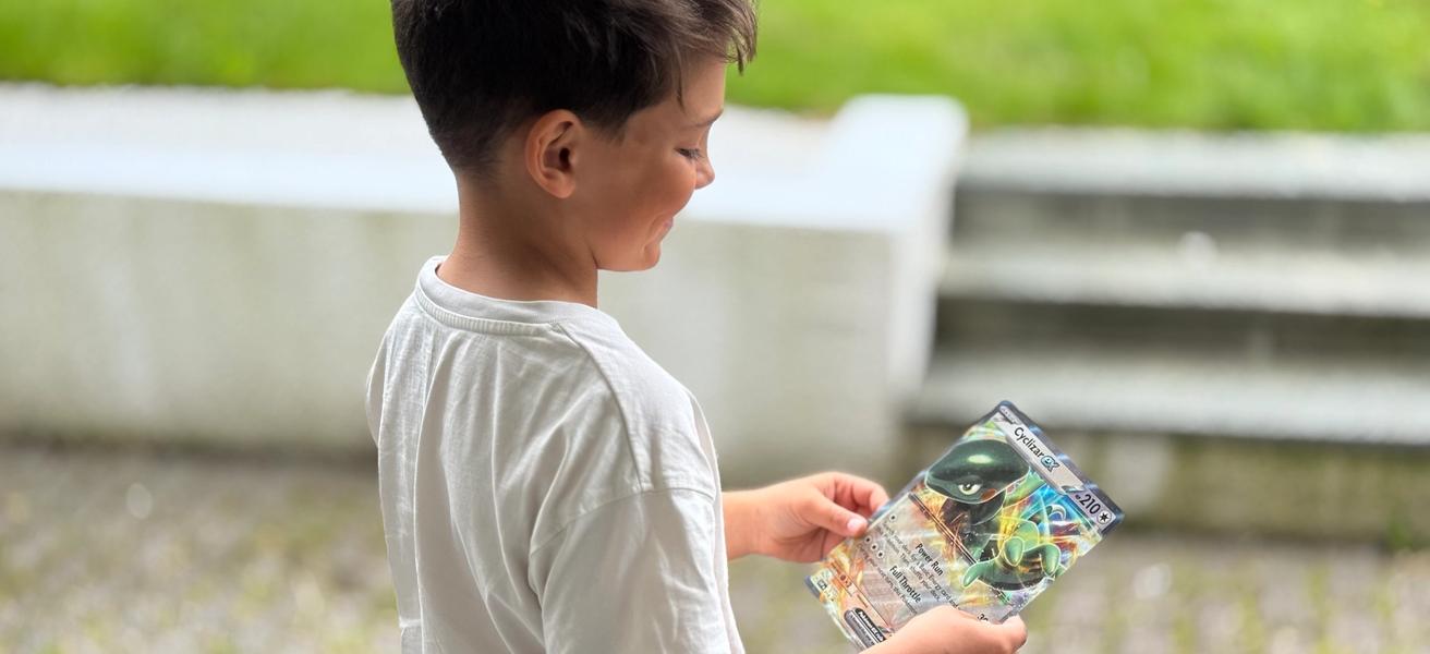 Gutt som står delvis med ryggen til kamera, holder et stor Pokemonkort.