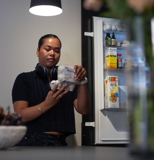 Ung kvinne som er ut av vinduet med kaffi i hånden, moderne leilighet i by.
