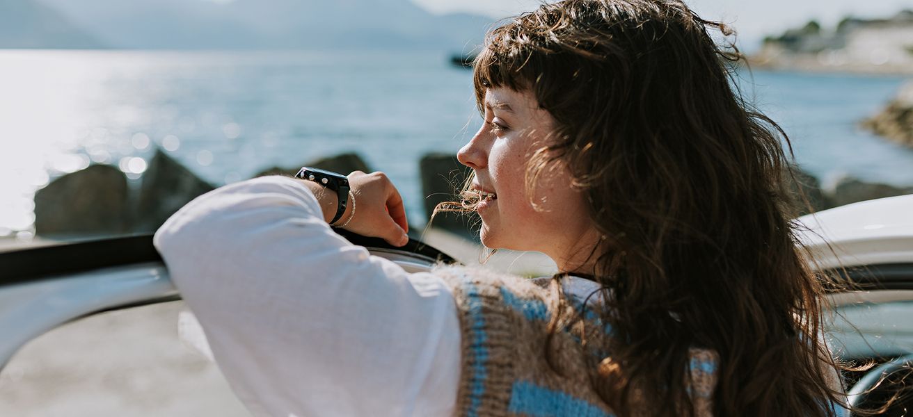 Dame som lener seg til bildør og ser utover fjorden.