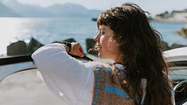 Dame som lener seg til bildør og ser utover fjorden.