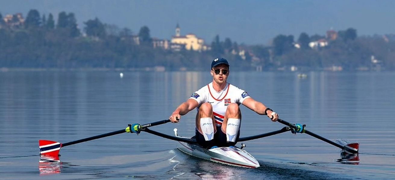 Martin Helseth som ror med fjell og bebyggelse i bakgrunn