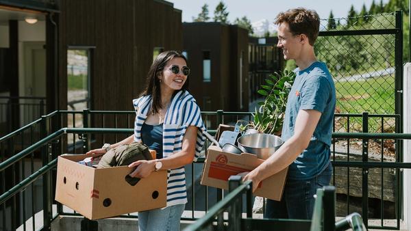 To unge mennesker, jente og gutt, som holder hver sin flyttekasse med saker og ting i.