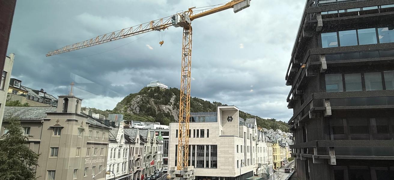 Sparebanken Møre sitt hovedkontor i Ålesund, med fjellstua i bakgrunn, og en stor kran i forkant.