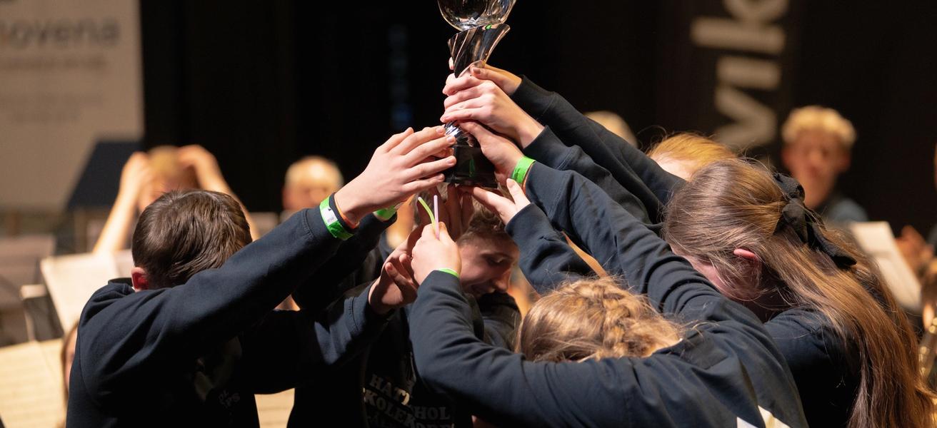 Ungdommer i mørke gensere står sammen og løfter en pokal