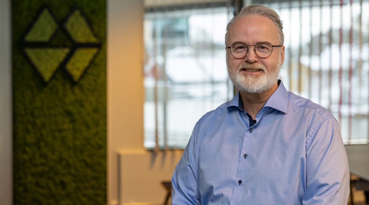 Mann med blå skjorte, briller og skjegg smiler til kamera