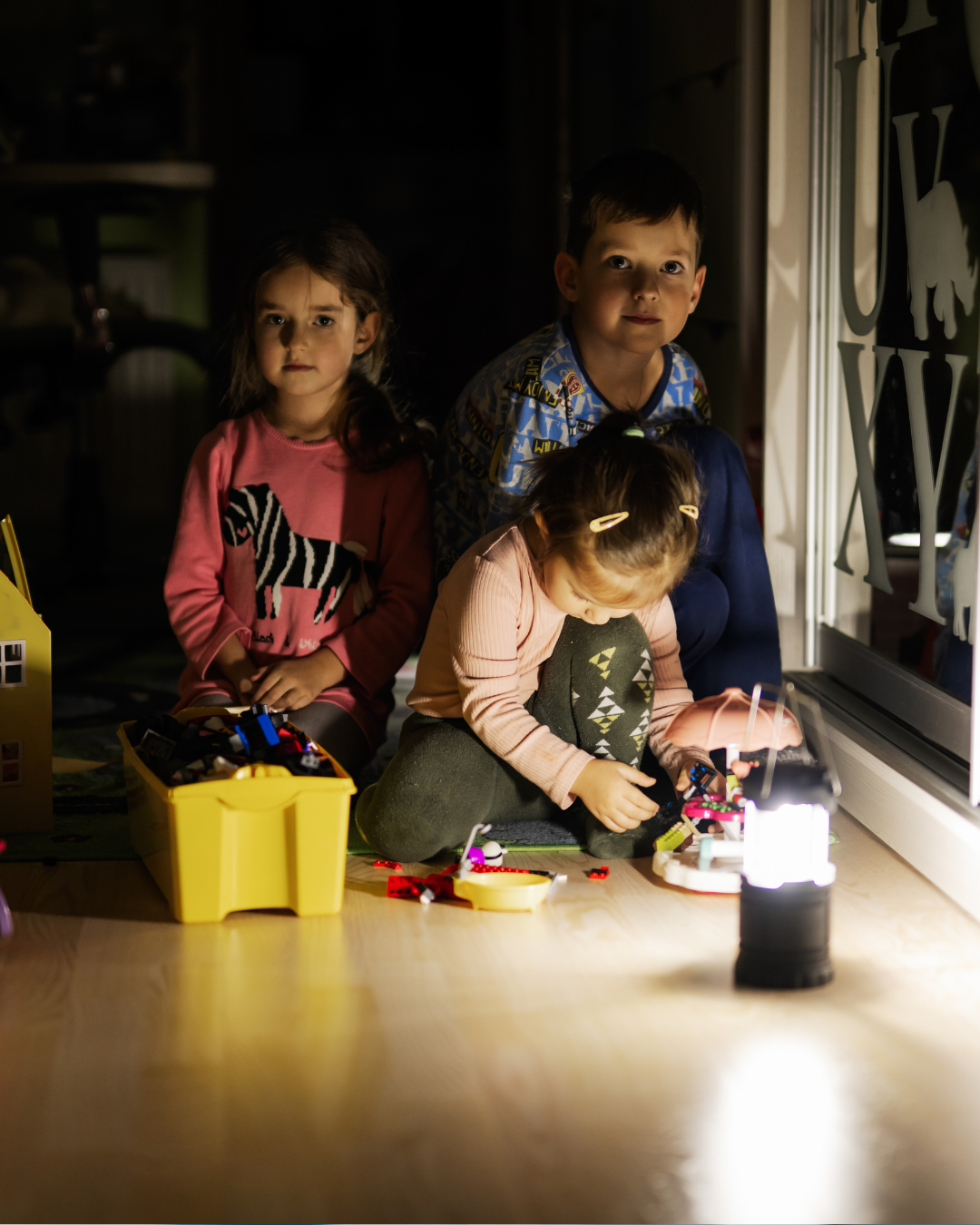Barn som sitter i mørket med en lampe foran seg. 
