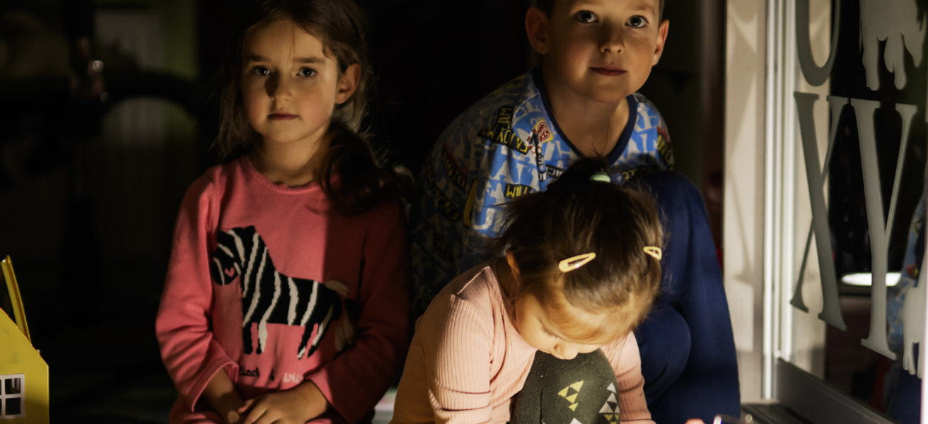 Barn som sitter i mørket med en lampe foran seg.