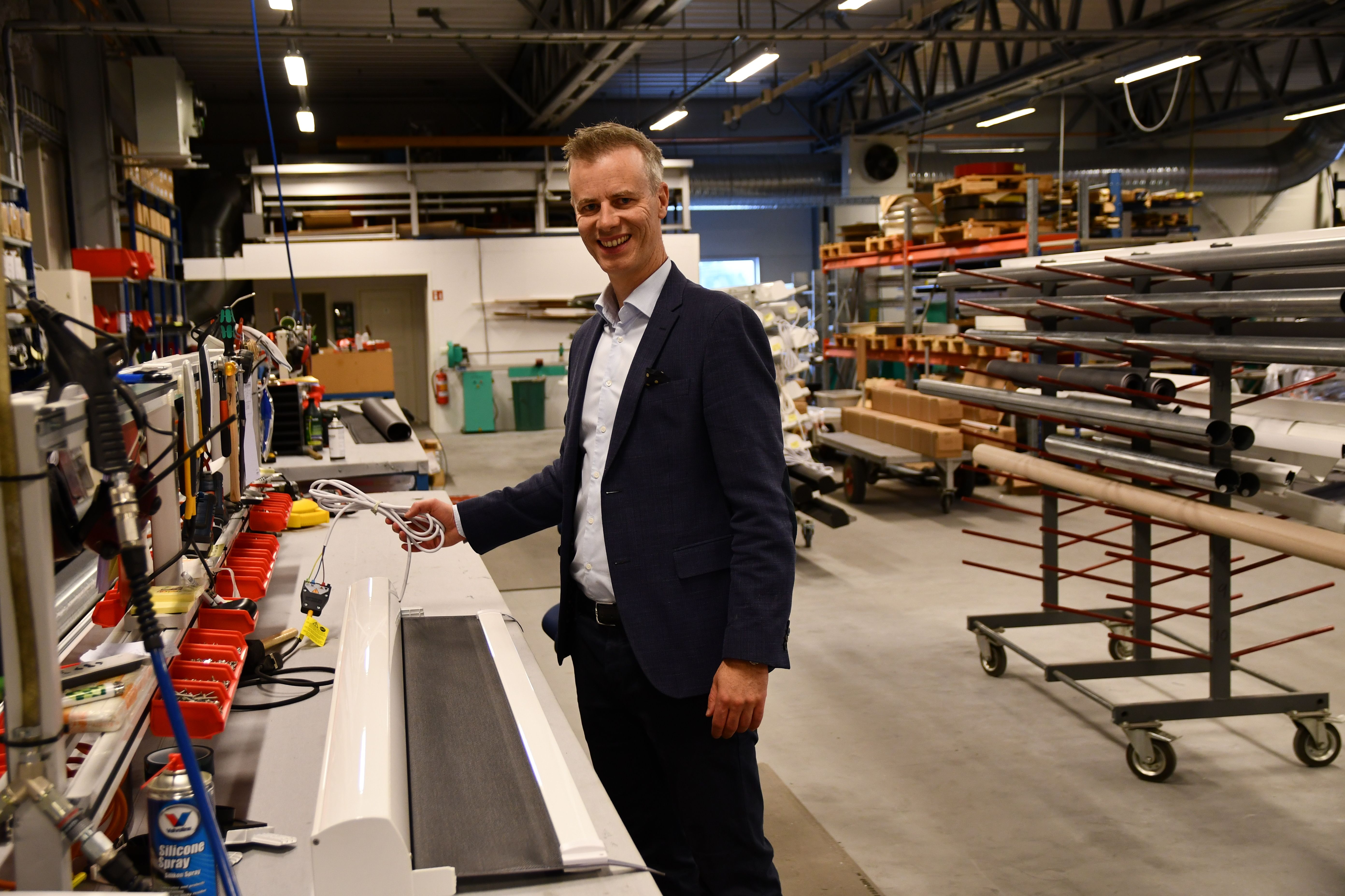 En mann står i produksjonslokalene hos Norsol, ved et arbeidsbord med solskjermingsprodukter og verktøy rundt seg.