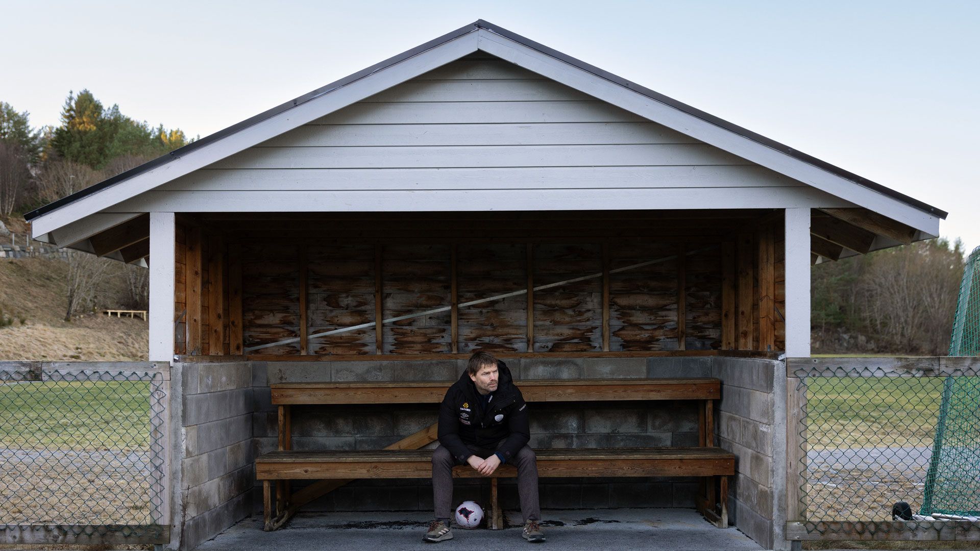 Mann sitter på en innbytterbenk på sidelinjen til en fotballbane.