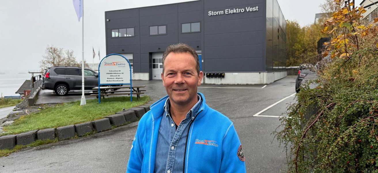 John Henry Holtet, grunnlegger av Storm Elektro smiler i kamera med Storm Elektro bygget i bakgrunnen