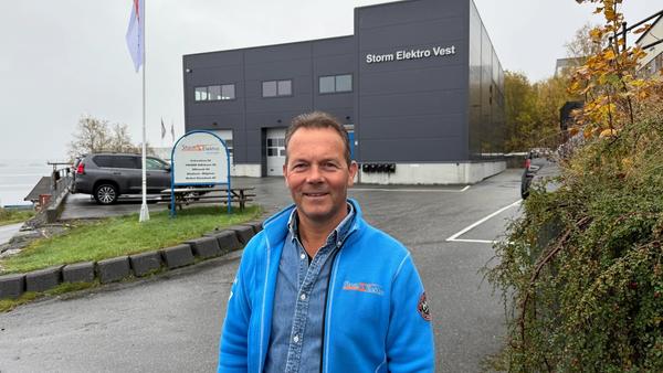 John Henry Holtet, grunnlegger av Storm Elektro smiler i kamera med Storm Elektro bygget i bakgrunnen