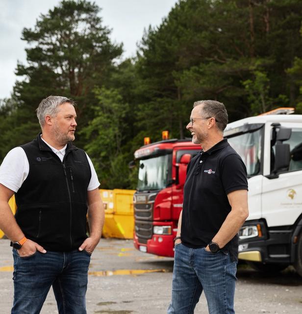 Henrik Wolmer og Odd Arve Hansen i samtale på området til Container Consult, med lastebiler og containere i bakgrunnen.