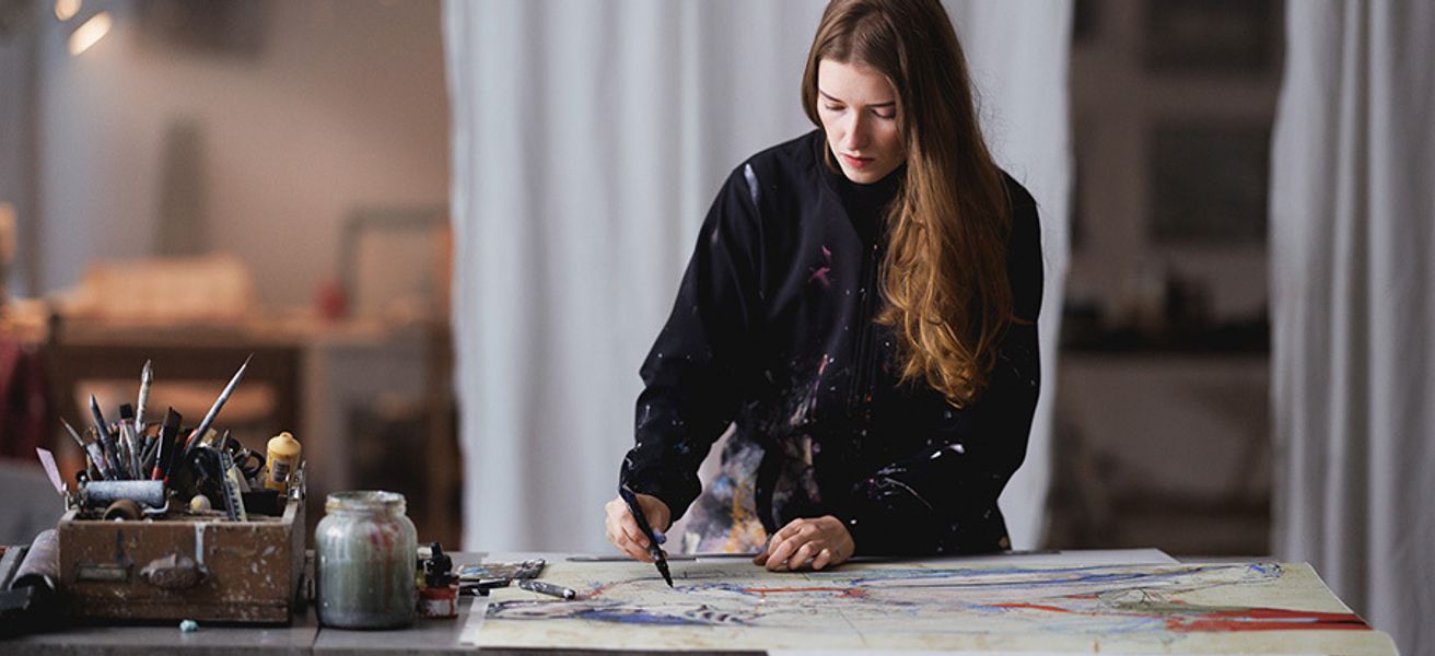 Ung kvinne arbeider med å håndkolorere et grafisk trykk i sitt atelier.