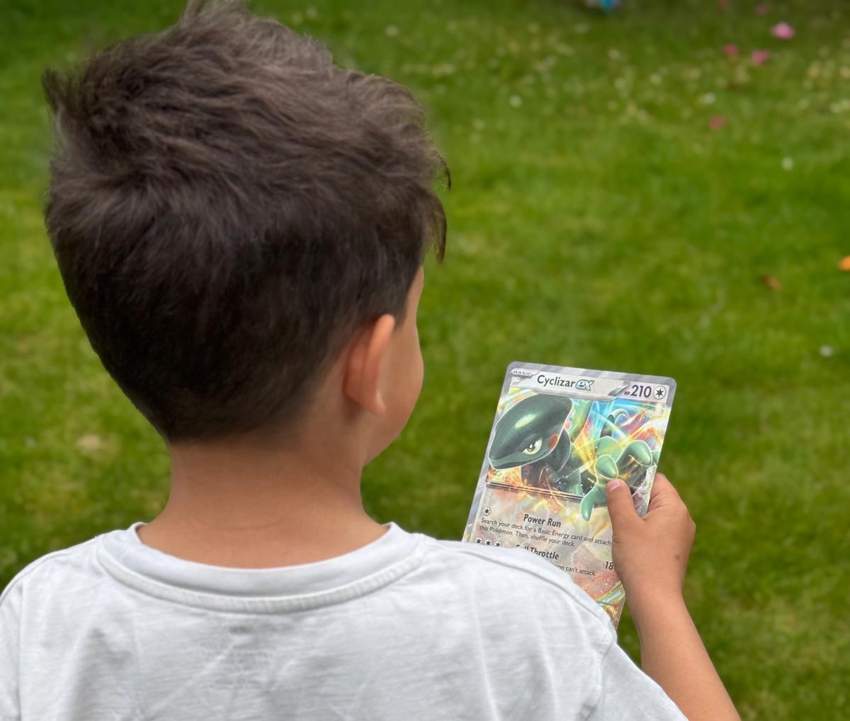 Gutt som står med ryggen til, holder et Pokemonkort i hånden.