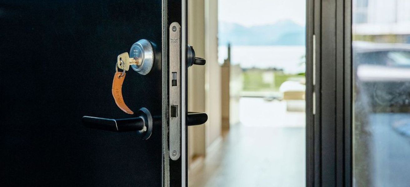 Åpen ytterdør med nøkkel i. Innsikt til moderne hus med utsikt mot fjord og fjell.