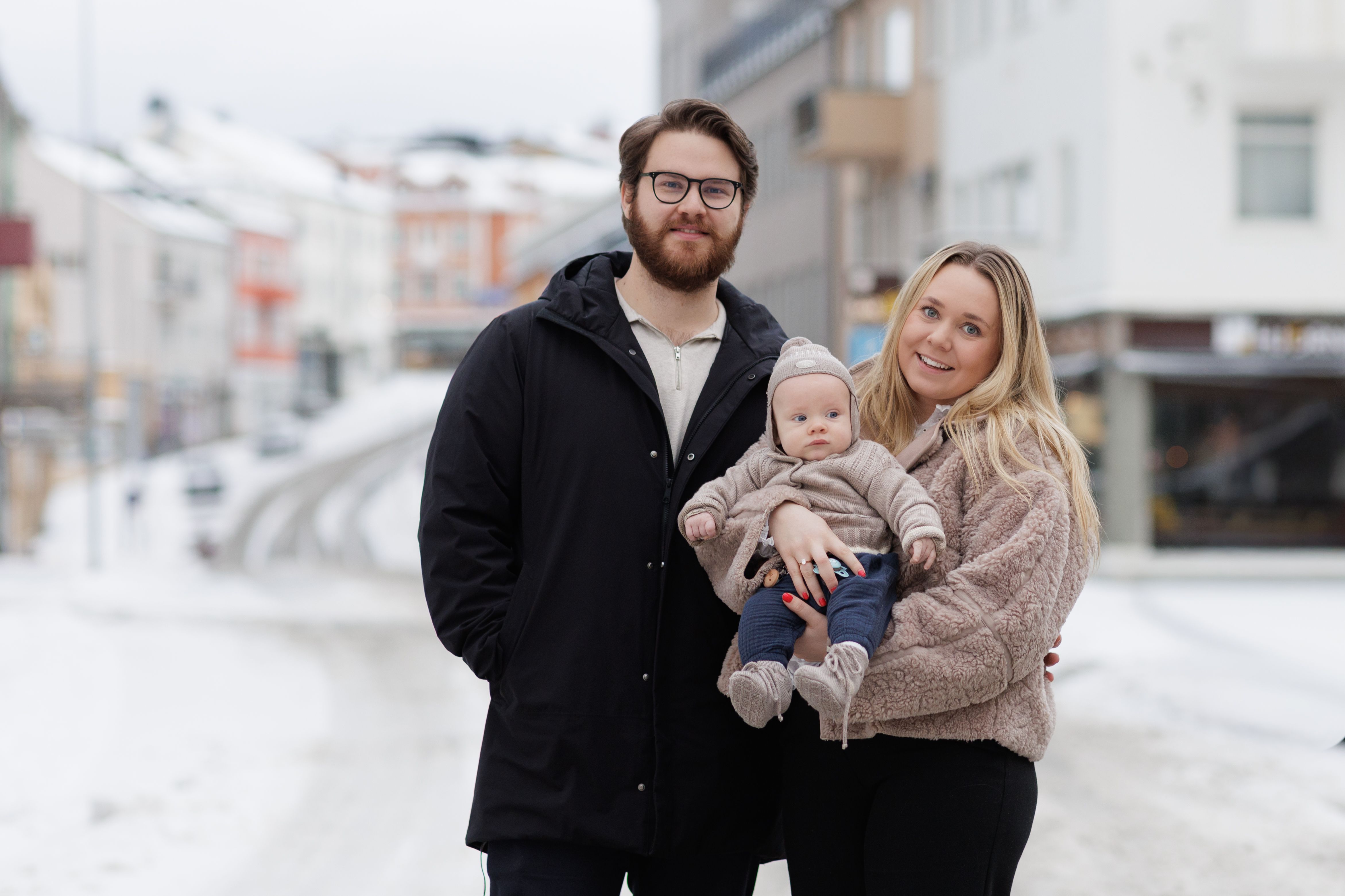 Ungt par i en vinterkledd gate med baby på hånden. 
