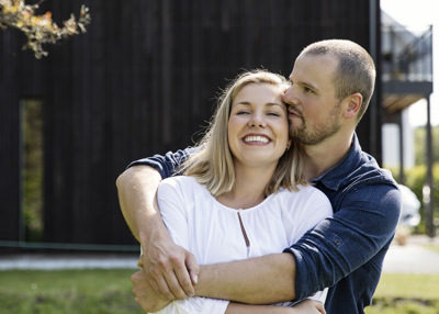 En mann holder kjærlig rundt en kvinne fremfor huset sitt. 