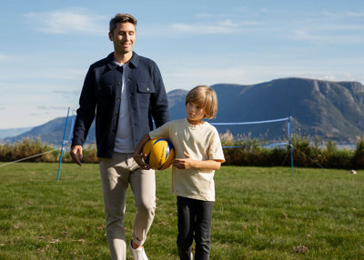 Far og ung sønn går på en gressplen. Sønnen holder en ball. 