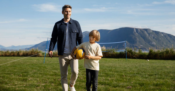 En voksen mann og en ung gutt går sammen ute på en gressplen. Gutten holder en gul ball.