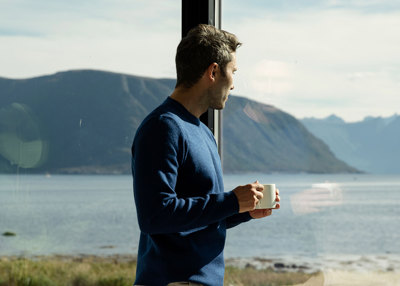Mann lener seg inn til et stort vindu, ser mot havet.