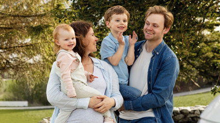 En familie på fire smiler til hverandre ute i naturen, en mor, far en liten gutt og en liten datter
