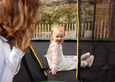 Liten jente sitter på en trampoline. Smiler. 