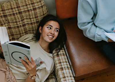 Kvinne ligger på en sofa, leser en bok.