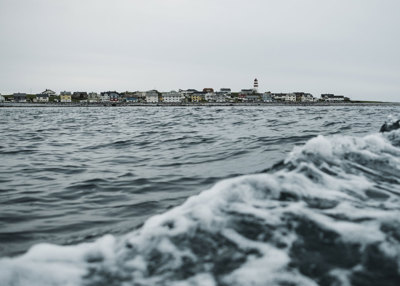 Bilde tatt fra havet. Ser en bølge og Alnes i bakgrunnen. 