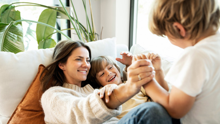 En mor som leker med sine to guttebarn i en sofa