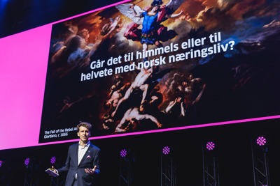 Runar Wiksnes i dress holder foredrag foran stor skjerm med kunstbilde og norsk tekst om norsk næringsliv.
