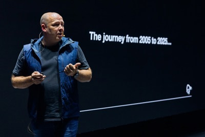 Bård Kvamme holder en presentasjon på scene foran en skjerm med teksten «The journey from 2005 to 2025...».