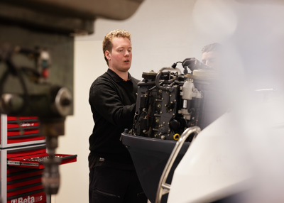 Thomas Risvik, daglig leder i Motorsenteret Ålesund arbeider med en båtmotor i et verksted, med verktøyskap i bakgrunnen.